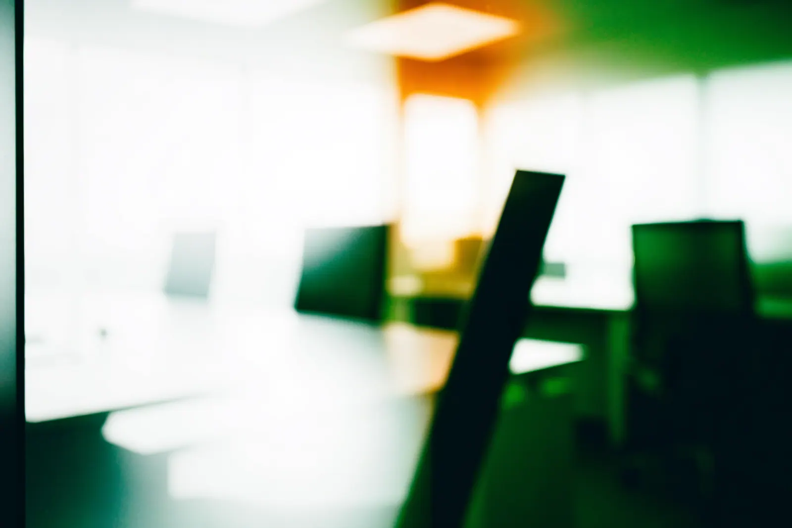 Sunlit office seen through frosted glass, desks and chairs reduced to soft green and stone shapes
